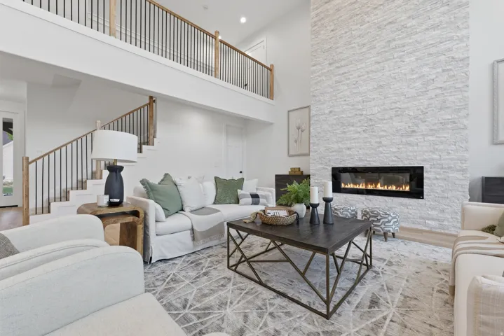 Two-story living area featuring a stacked stone fireplace with a linear insert, a grand staircase with wood newel posts and black metal balusters, and a second-story overlook