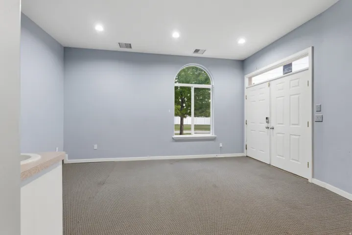 Spacious room featuring a prominent arched window, double entry doors with a transom window, recessed ceiling lighting, and light-colored carpeting