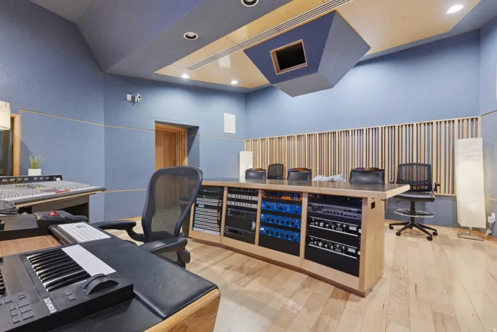 Dedicated studio space featuring acoustic paneling on walls and ceiling, wood-finish flooring, recessed lighting, a built-in sound mixing desk with integrated equipment racks, and a wood slat acoustic wall treatment
