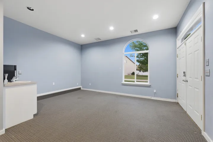 Spacious interior room featuring a large arched window, recessed lighting, and a built-in wet bar with a sink and countertop