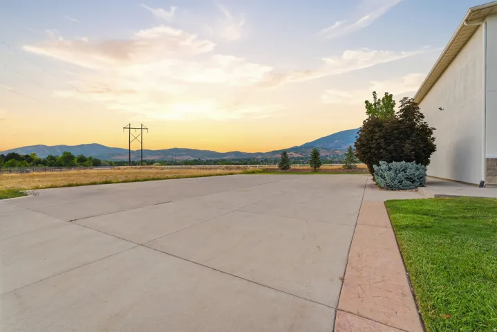Expansive concrete paving with a landscape border, manicured lawn, and mature plantings