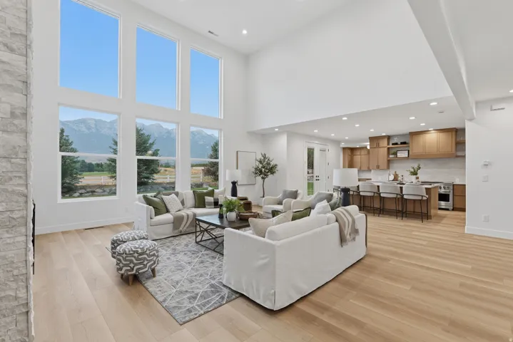Vaulted great room featuring tall windows with mountain scenery, light wood-finish flooring, and a stone-clad fireplace