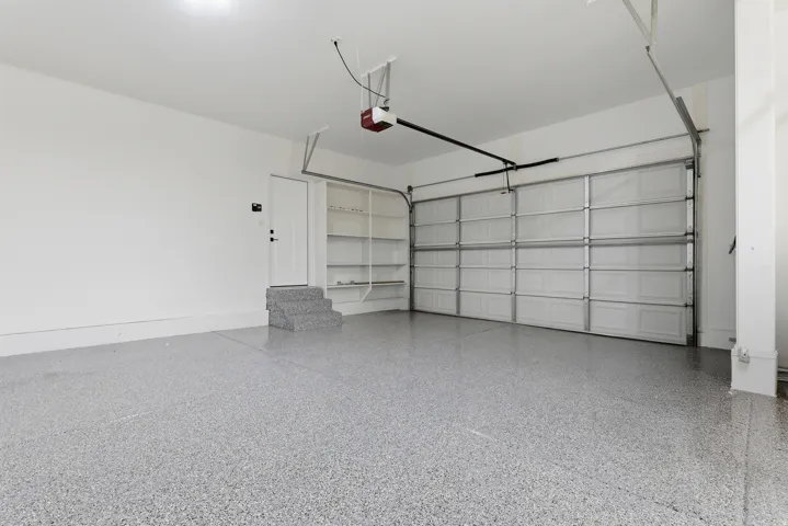 Spacious garage featuring a durable epoxy-coated floor, automatic garage door opener, built-in shelving, and a service door for interior access
