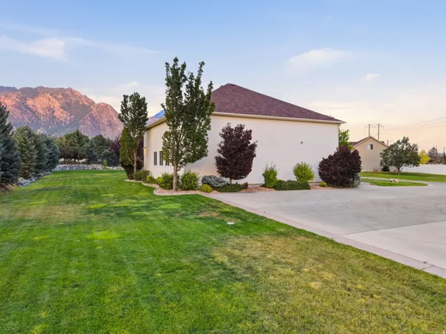 Spacious exterior featuring a light-colored facade, brown shingle roof, extensive green lawn, mature trees, and a concrete driveway