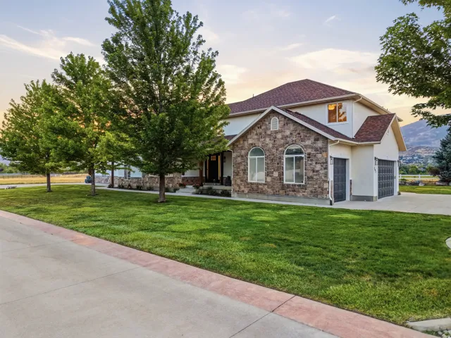 Stone and stucco exterior with an attached garage, featuring a concrete driveway and mature trees bordering a manicured lawn