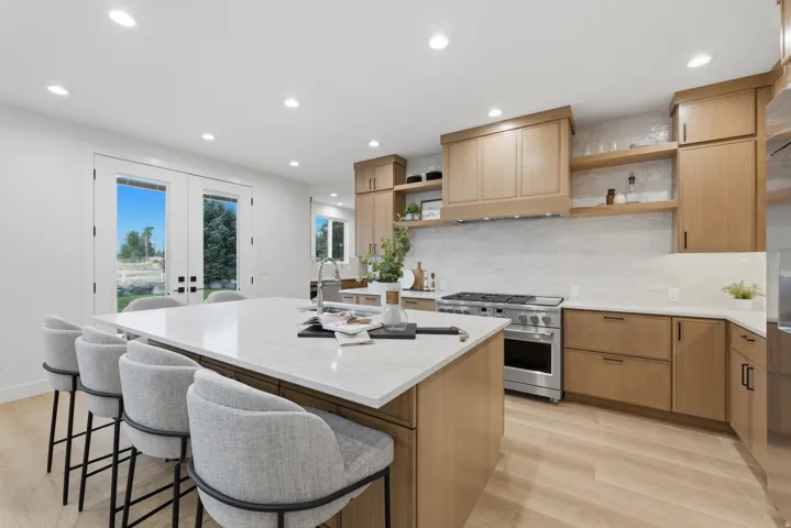 Kitchen featuring a large central island with a sink, light wood-finish cabinetry, stainless steel range with matching hood, light stone countertops, and recessed lighting