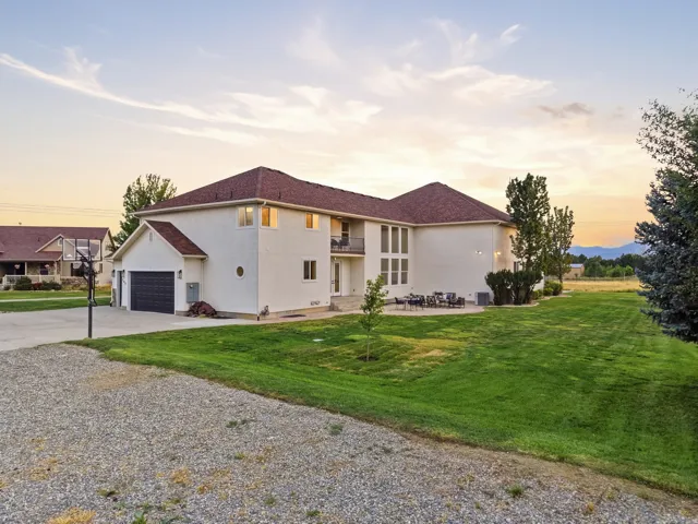 Spacious two-story residence featuring a gravel driveway, attached garage, large rear patio, and expansive green lawn