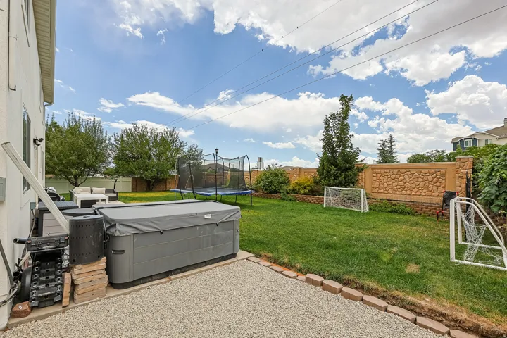 Backyard featuring a covered hot tub on a gravel patio, leading to a lawn area