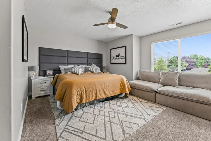 Carpeted room featuring a large window, a ceiling fan, and a paneled headboard
