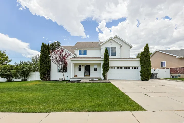 Two-story stucco residence featuring a two-car garage, mature landscaping, and a covered entry