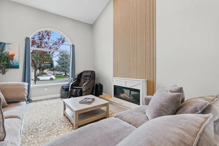 Vaulted ceiling living space featuring an arched window, a built-in fireplace with a white mantel, and a vertical wood slat accent wall