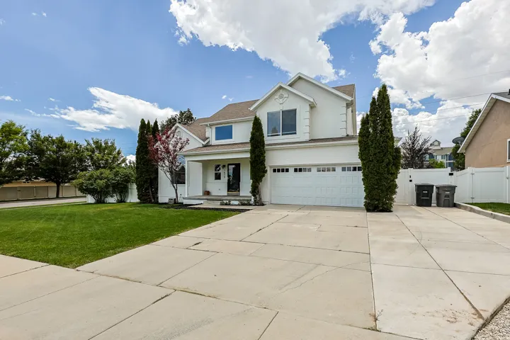 Two-story stucco residence featuring a two-car garage, mature landscaping, and a concrete driveway