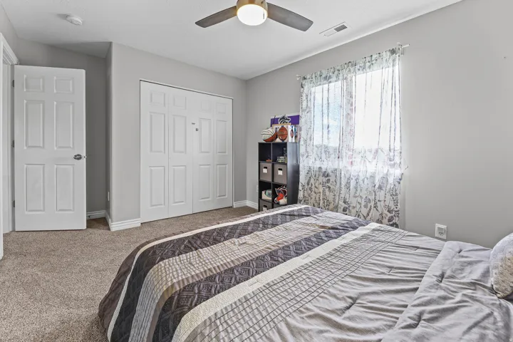 Carpeted interior room featuring a window with patterned curtains, a ceiling fan with integrated lighting, a six-panel interior door, and a bi-fold closet door