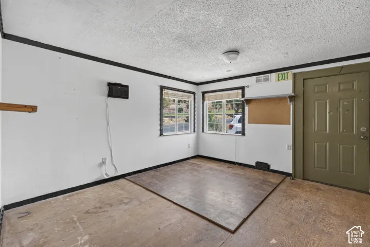 Versatile interior space featuring two windows with horizontal blinds, a paneled door, and a textured ceiling