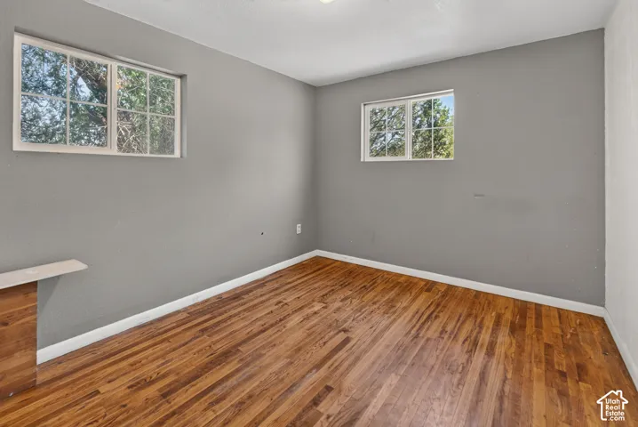 Room featuring two windows, wood-finish flooring, light gray wall paint, white baseboards, and a built-in wood-finish cabinet with a light-toned top