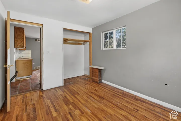 Room featuring wood-finish flooring, a double-hung window, and an open closet with shelving and hanging rod