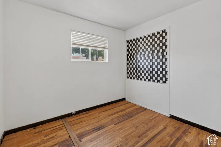Room featuring wood-finish flooring, white walls, and a window with blinds