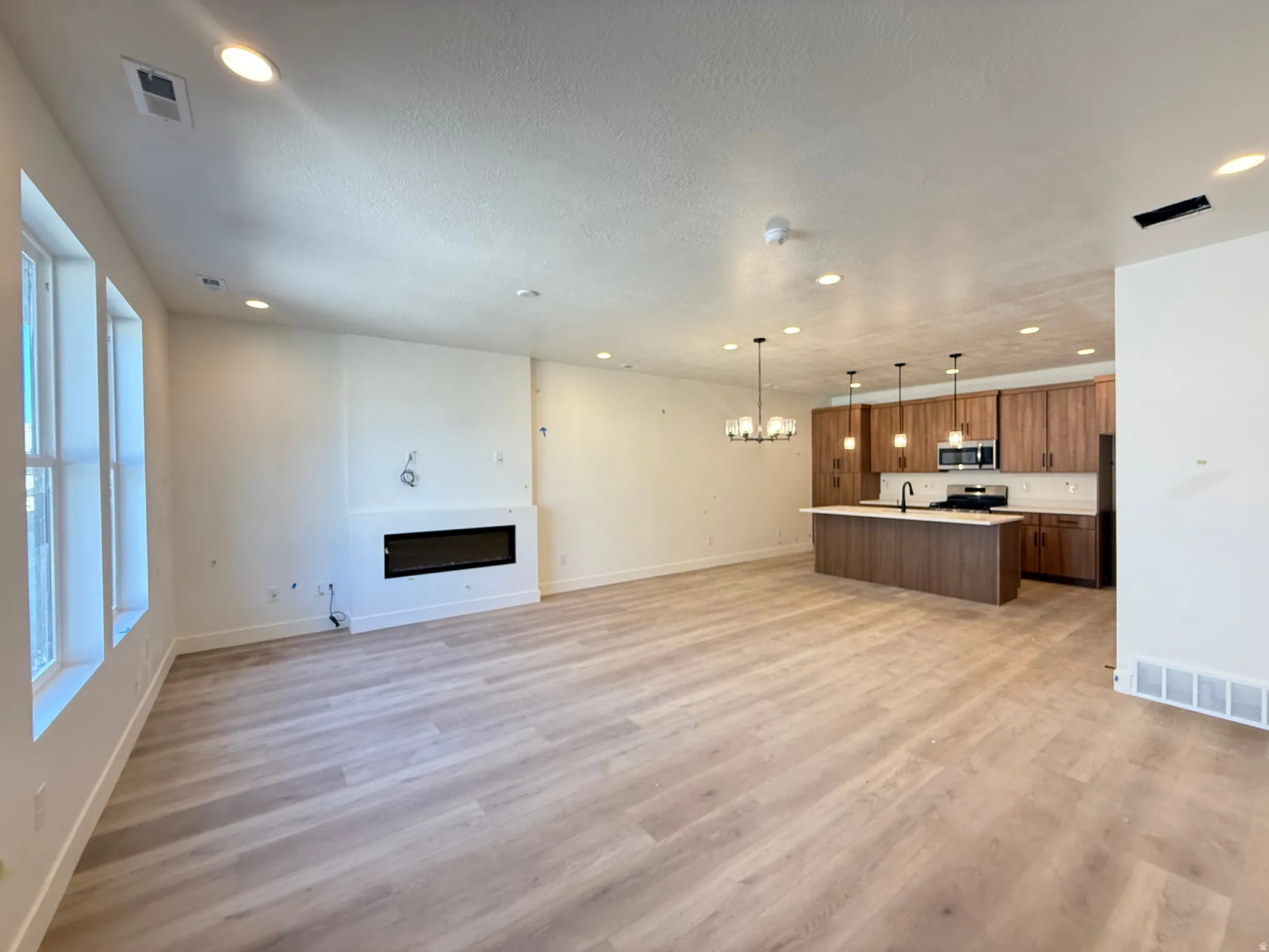 Open-concept living space featuring wood-finish flooring, a modern electric fireplace, recessed lighting, and a kitchen island with pendant lighting