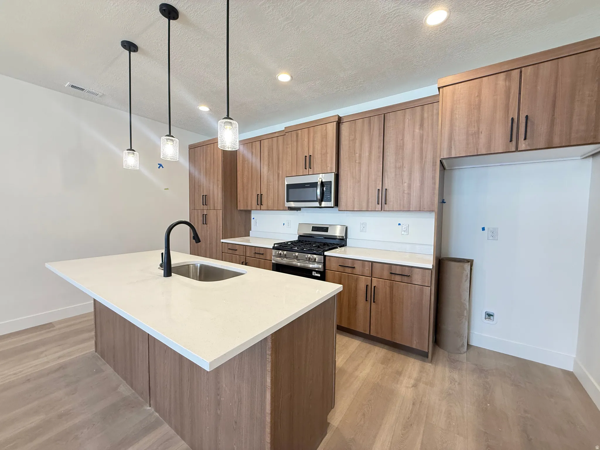 Kitchen featuring a central island with a stainless steel sink, solid surface countertops, wood-finish cabinetry, stainless steel appliances, and pendant lighting