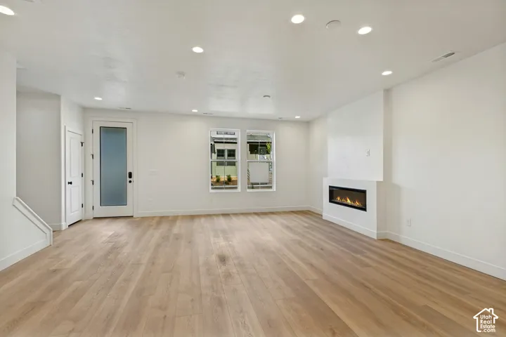 Open interior space featuring light wood-finish flooring, recessed lighting, a modern linear fireplace, and an exterior door with frosted glass inlay