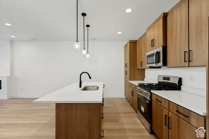 Kitchen featuring wood-finish cabinetry, white countertops, a center island with a stainless steel sink and matte black faucet, and three pendant lights
