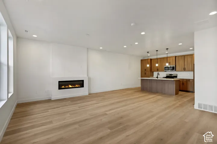 Open concept interior featuring wood-finish flooring, recessed lighting, built-in linear fireplace, kitchen island with countertop seating, and wood-finish cabinetry