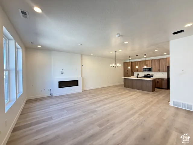 Open-concept living space featuring wood-finish flooring, a modern electric fireplace, recessed lighting, and a kitchen island with pendant lighting
