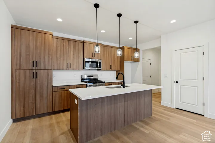 Kitchen featuring flat-panel wood-finish cabinetry, light-toned stone countertops, a central island with an integrated sink, matte black hardware, and trio of pendant lights