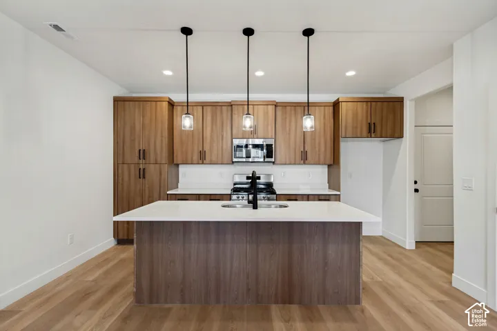Kitchen featuring wood-finish cabinetry, an expansive central island with a quartz countertop, stainless steel appliances, and three pendant light fixtures