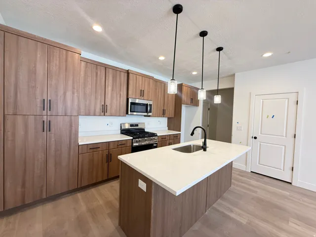Contemporary kitchen featuring a center island, wood-finish cabinetry, stainless steel appliances, white countertops, and pendant lighting