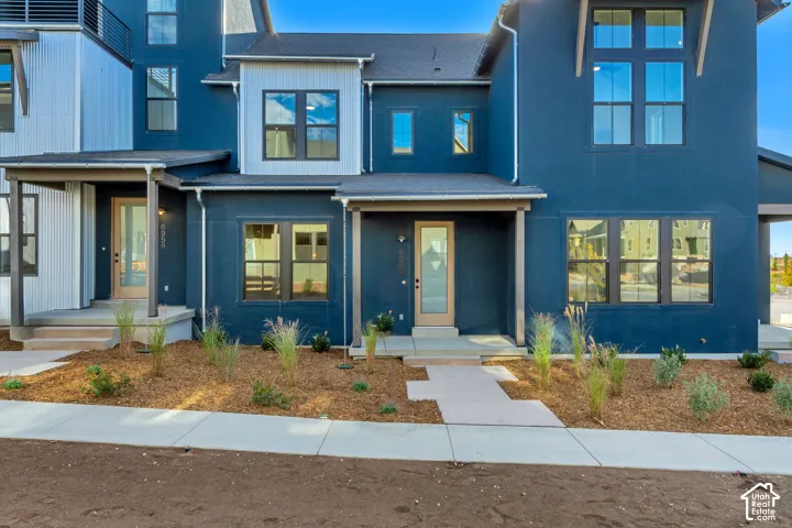 Modern two-story exterior featuring smooth-finish dark blue siding, light wood-toned entry doors, multi-pane windows with dark framing, and a metal roof accent