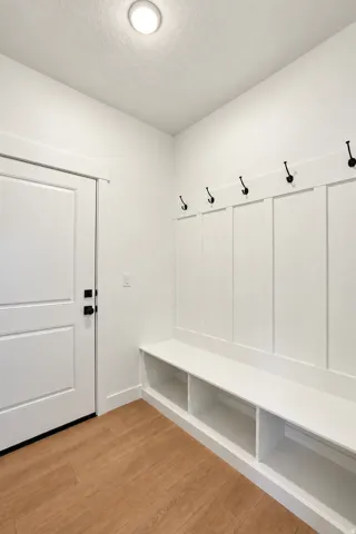 Recessed ceiling light, white paneled walls, built-in storage bench, wood-finish flooring, and a white panel door with black hardware
