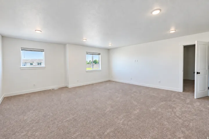 Recessed lighting illuminating a spacious room with light-colored carpeting, multiple windows providing natural light, and a white interior door