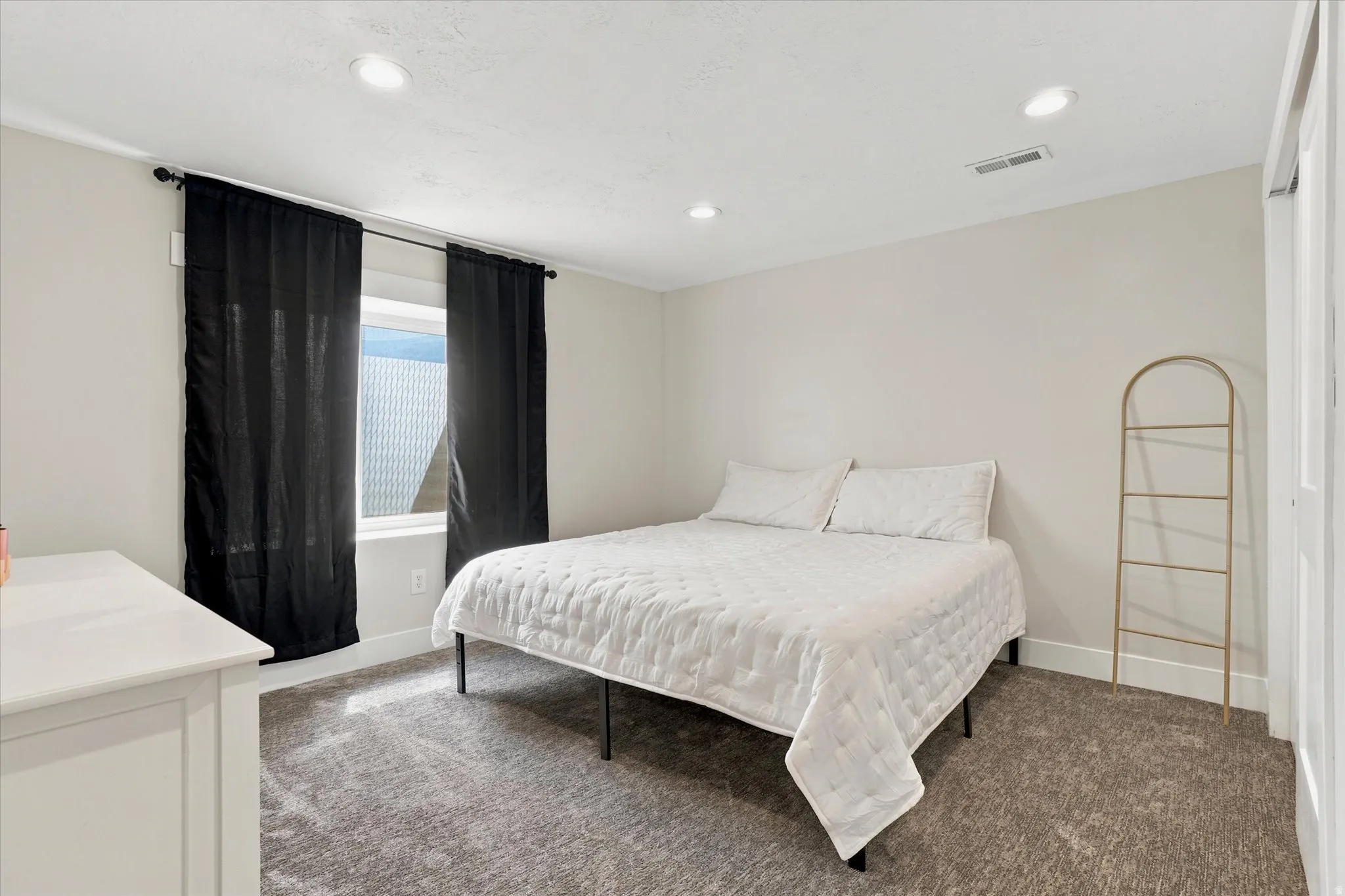 Carpeted room featuring a window with black curtains, recessed lighting, and a white dresser