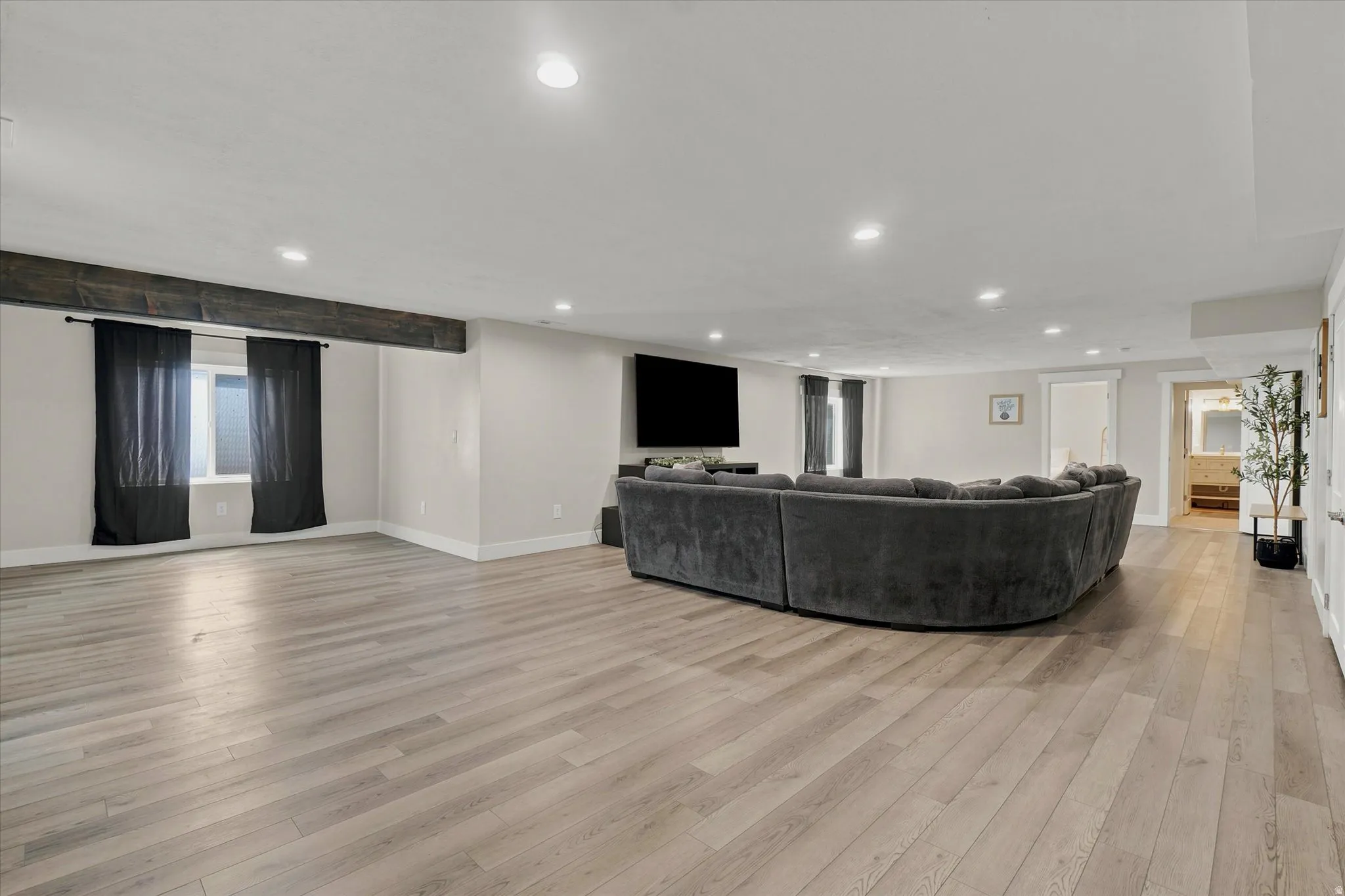 Spacious living area featuring wood-finish flooring, recessed lighting, and a prominent dark wood beam accent