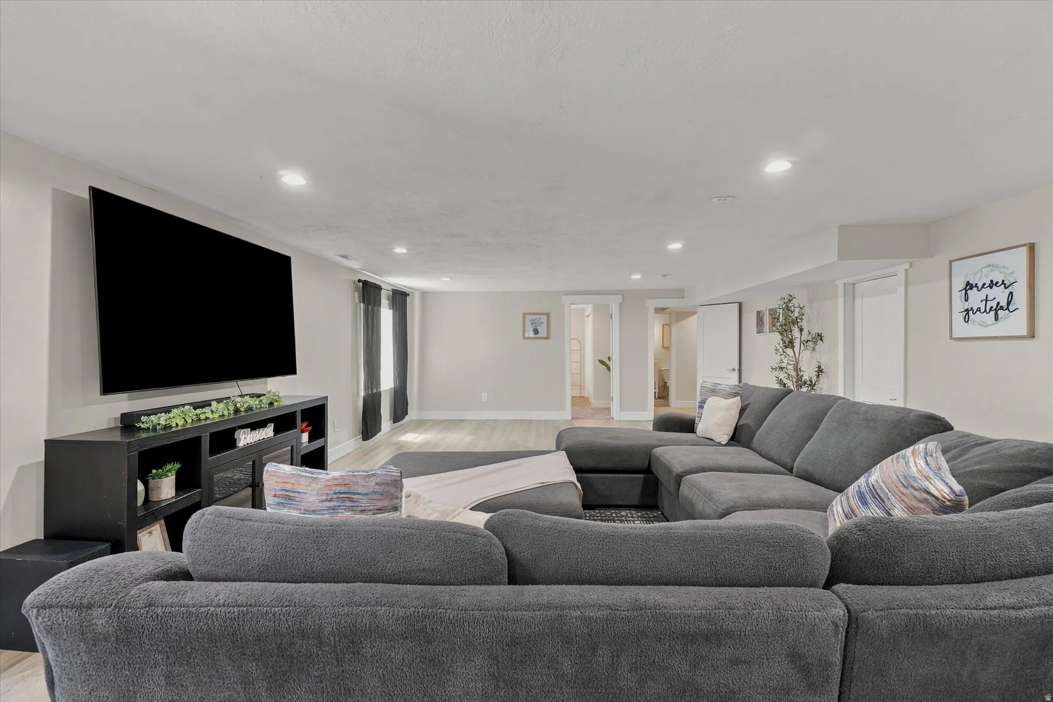 Spacious living area featuring light-toned walls, recessed lighting, wood-finish flooring, and white trim