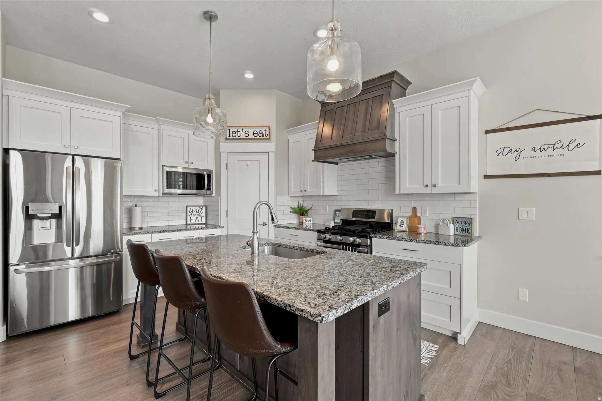 Kitchen featuring a large island with a composite countertop, white shaker cabinetry, stainless steel appliances, and wood-finish flooring