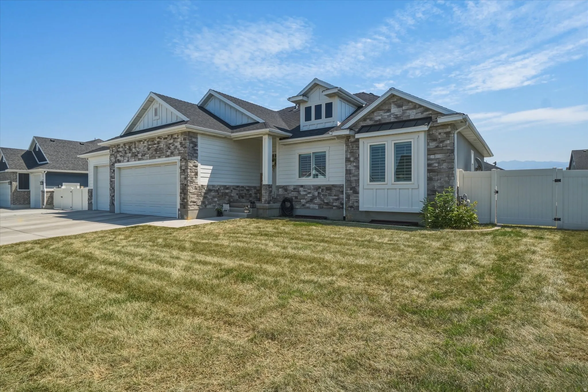 Modern home exterior with stacked stone accents, horizontal siding, a two-car garage, and a white privacy fence