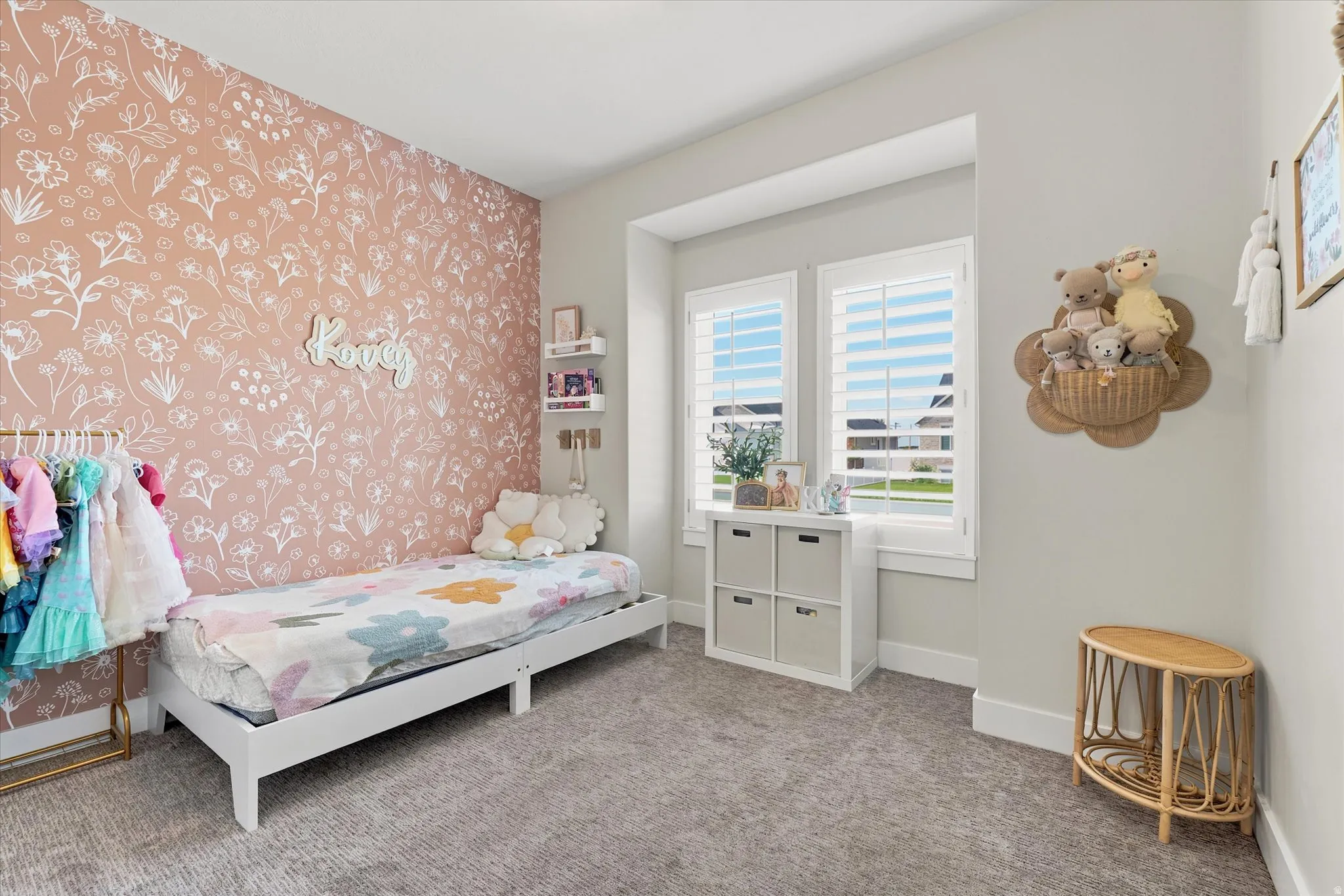 Bedroom featuring a floral accent wall, plush carpeting, and dual windows with plantation shutters