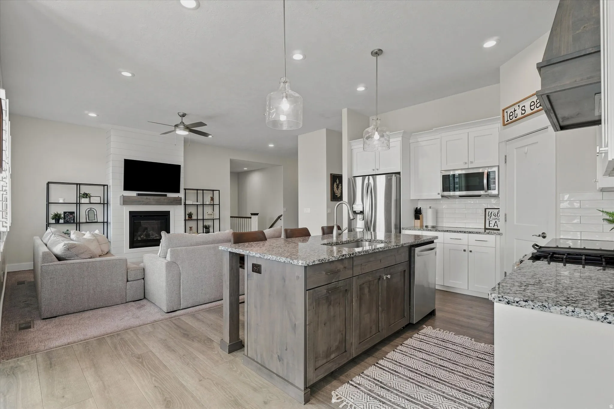 Open-concept living space featuring a kitchen island with seating, pendant lighting, stainless steel appliances, and wood-finish flooring