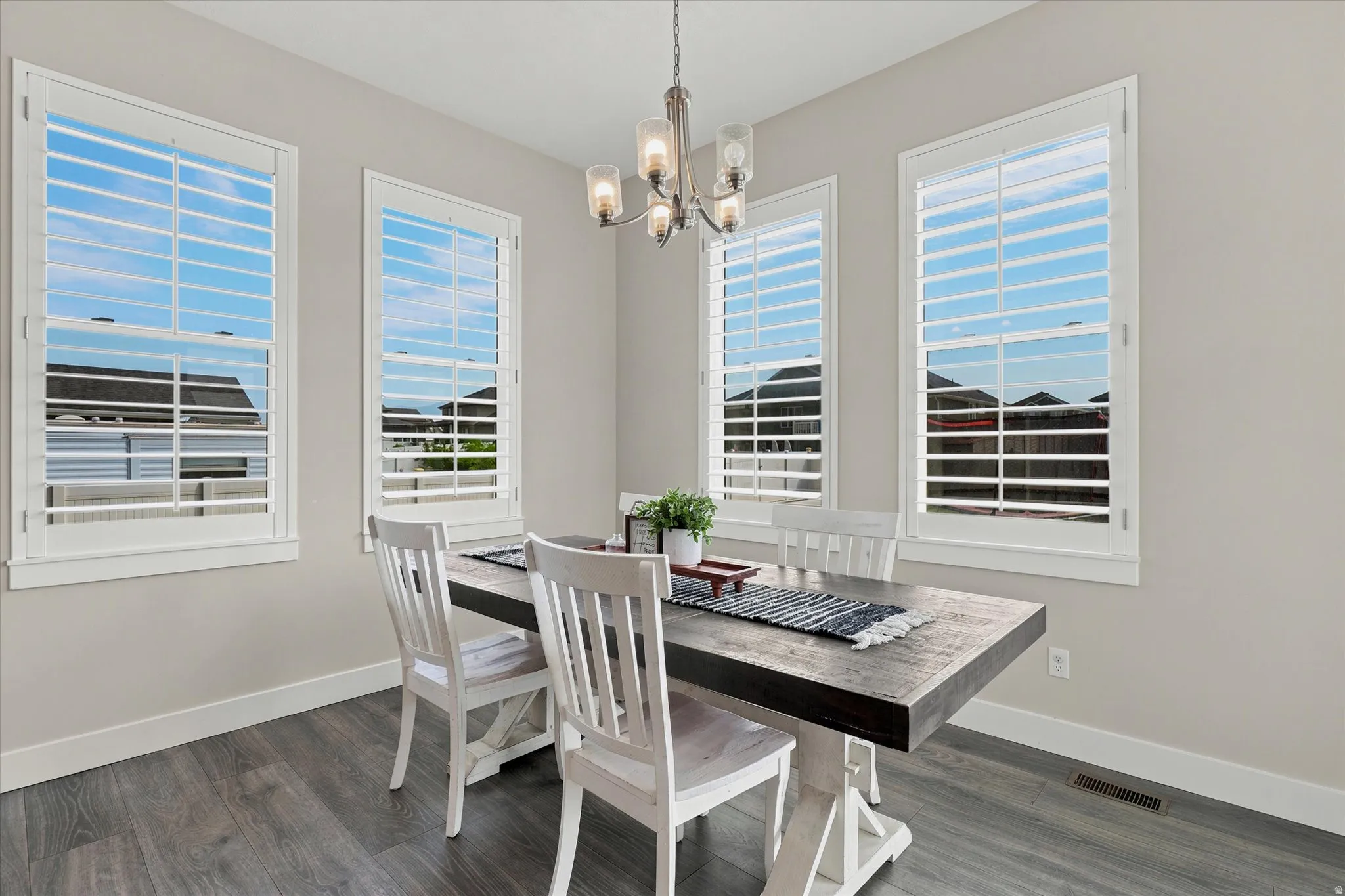 Dining area with four windows featuring white plantation shutters, wood-finish flooring, and a chandelier with glass shades
