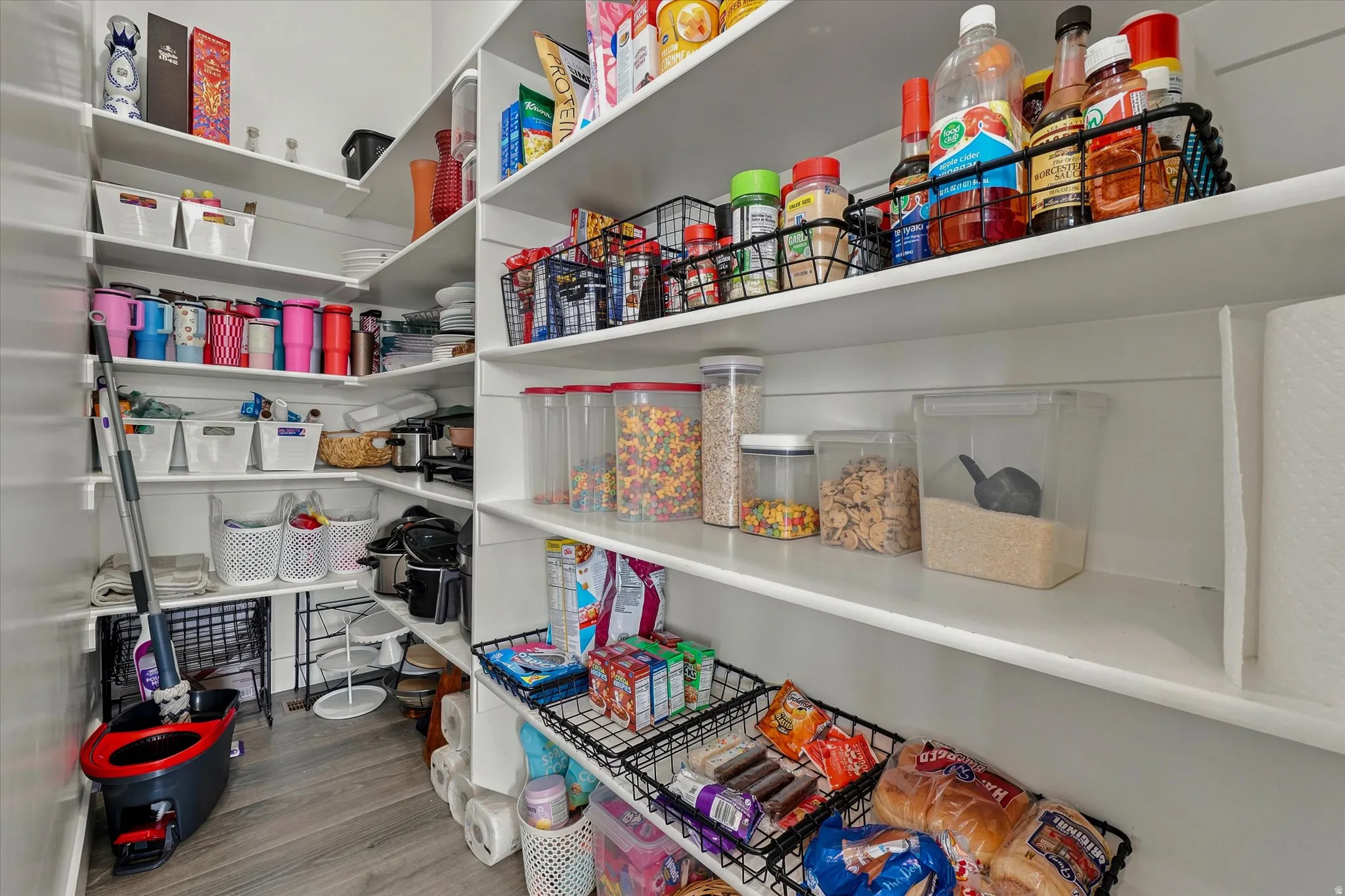 Spacious walk-in pantry featuring extensive white shelving and wood-finish flooring