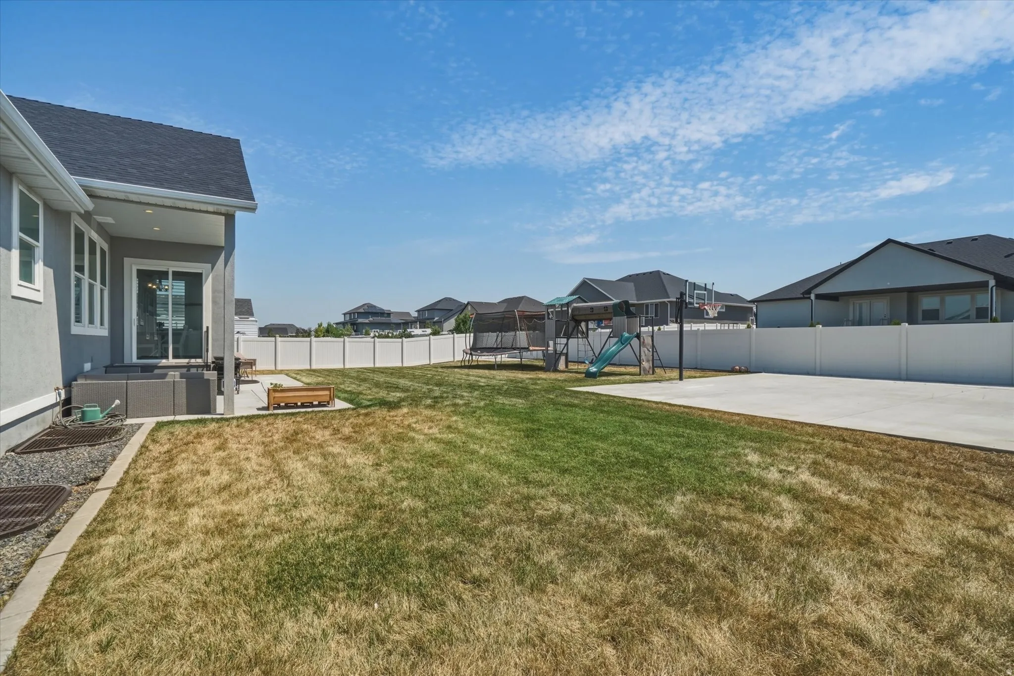 Expansive backyard featuring a concrete patio, sliding glass door access, and a white vinyl privacy fence