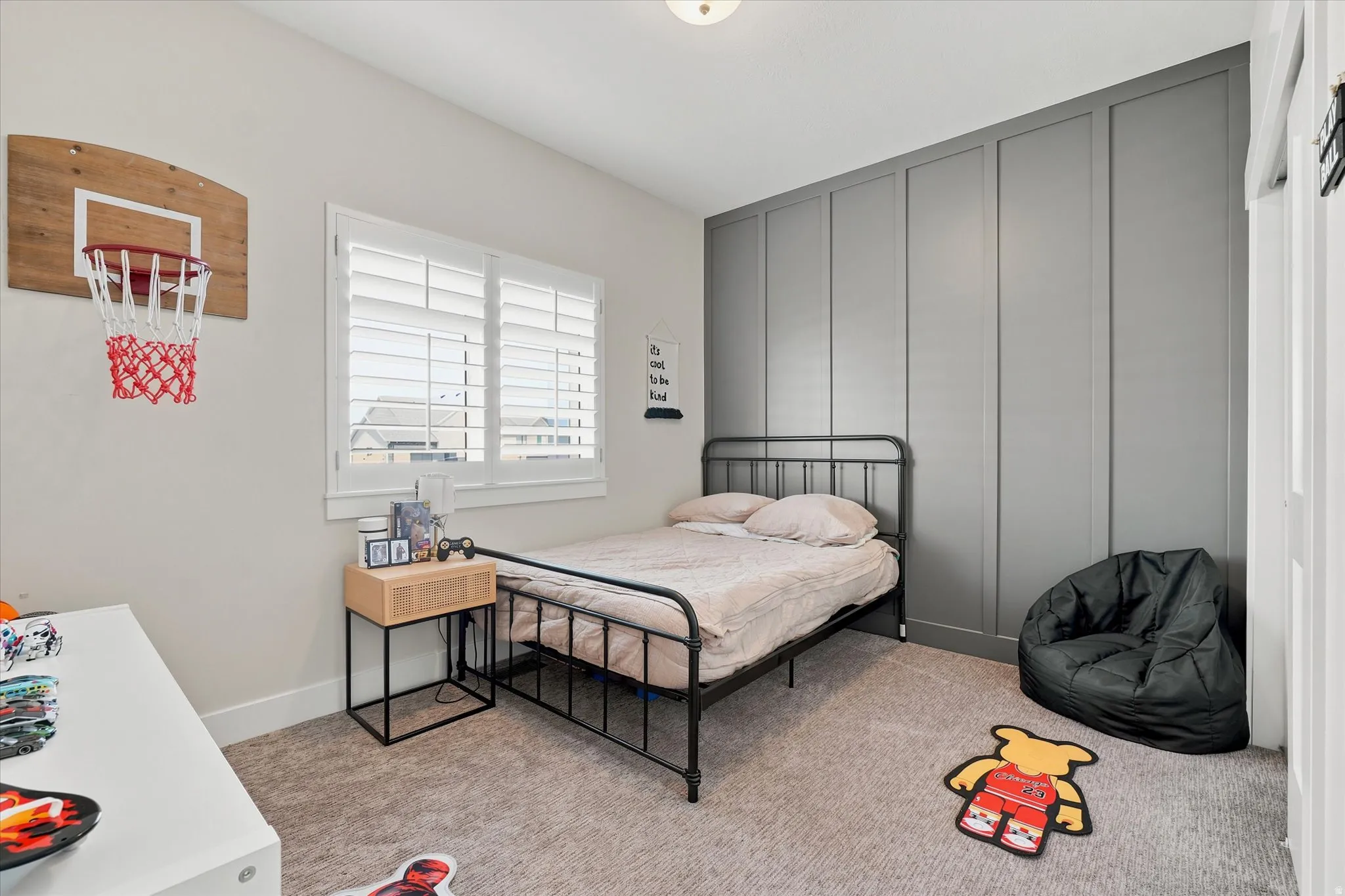 Bedroom featuring a paneled accent wall, neutral carpeting, and a window with plantation shutters
