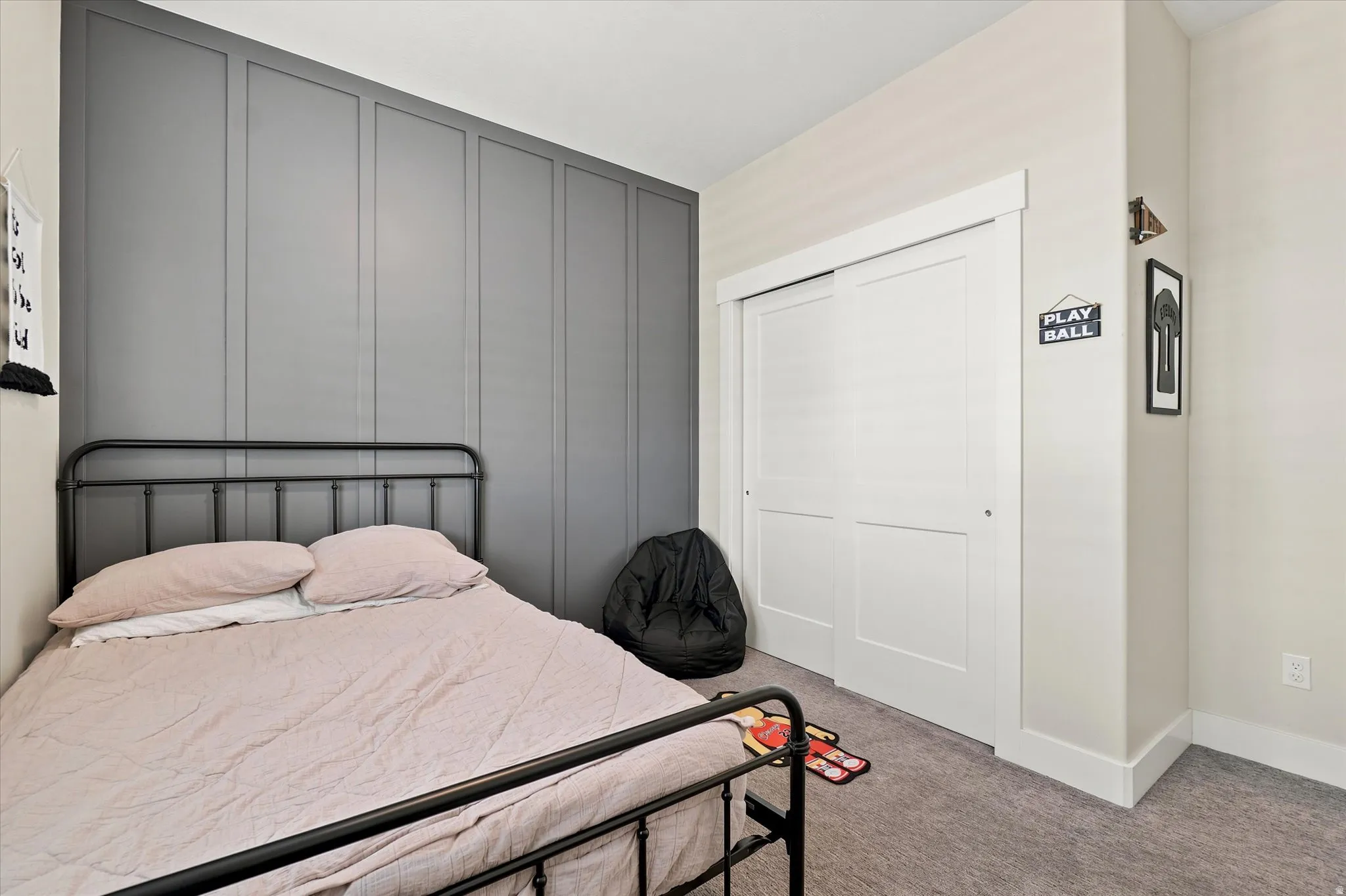 Bedroom featuring a gray accent wall with vertical paneling, light neutral wall paint, white trim, and gray carpeting
