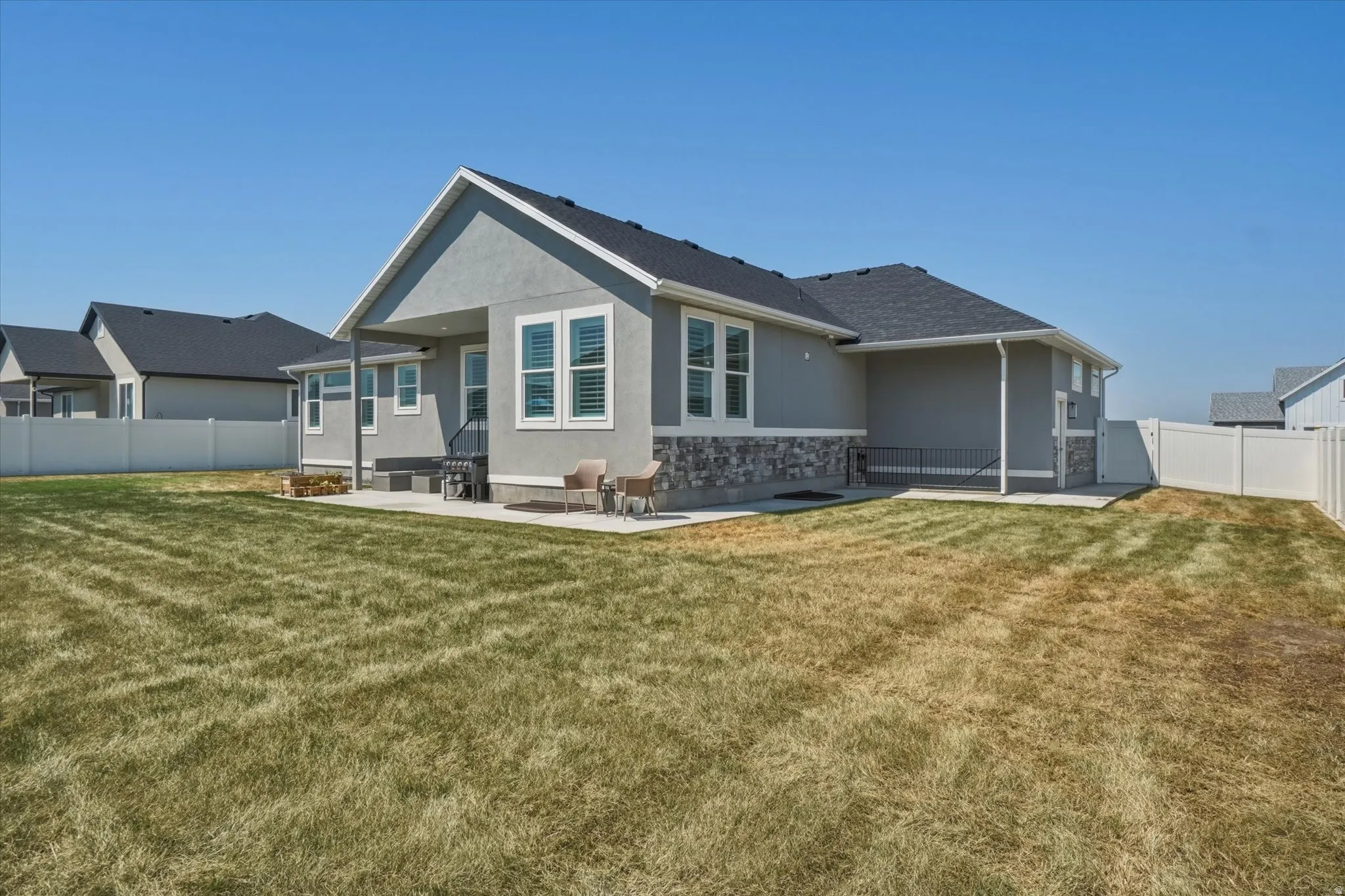 Spacious backyard featuring a concrete patio, stucco exterior with stone accents, and a privacy fence