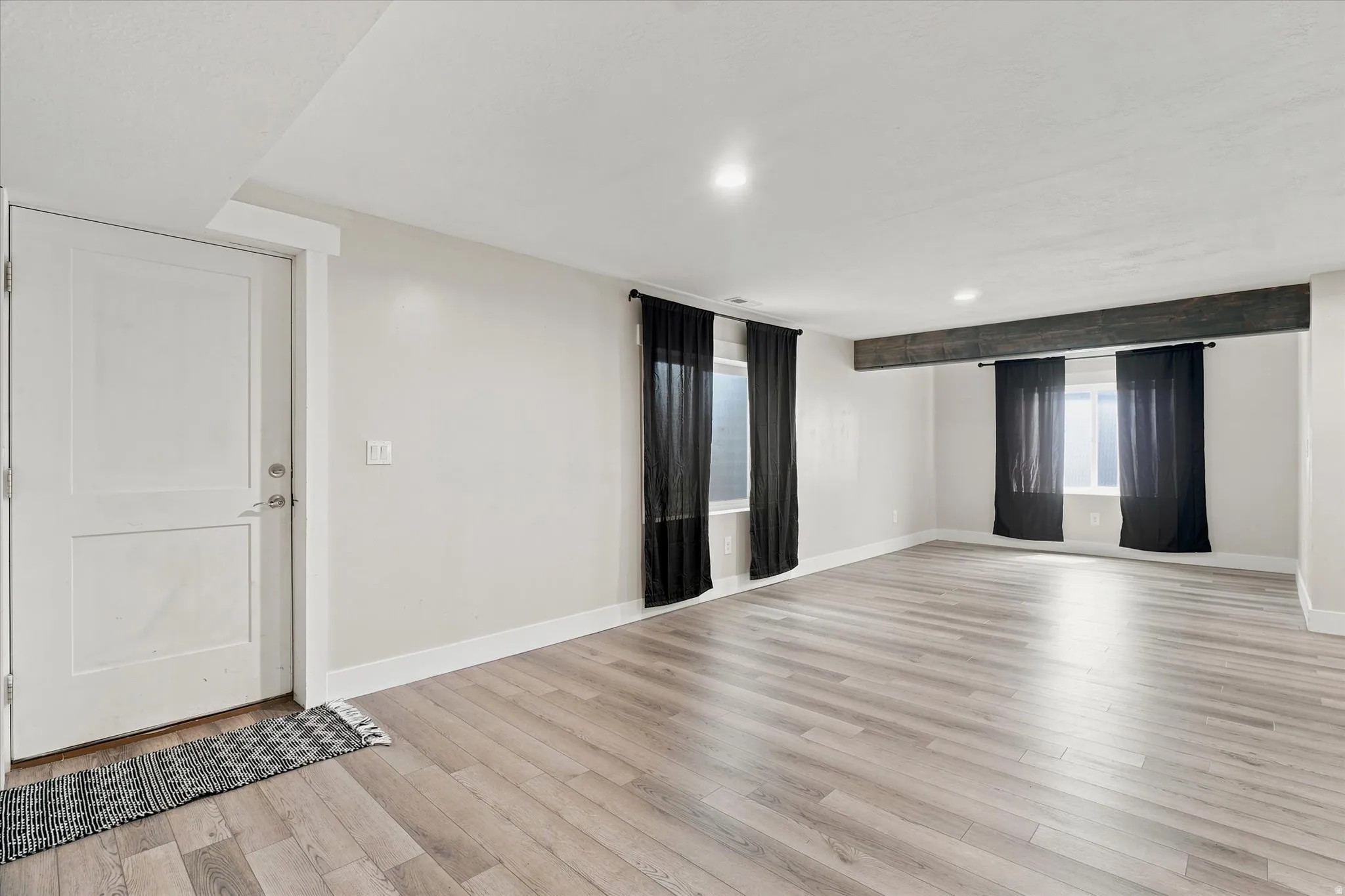 Spacious room featuring light wood-finish flooring, recessed lighting, and a prominent exposed beam detail