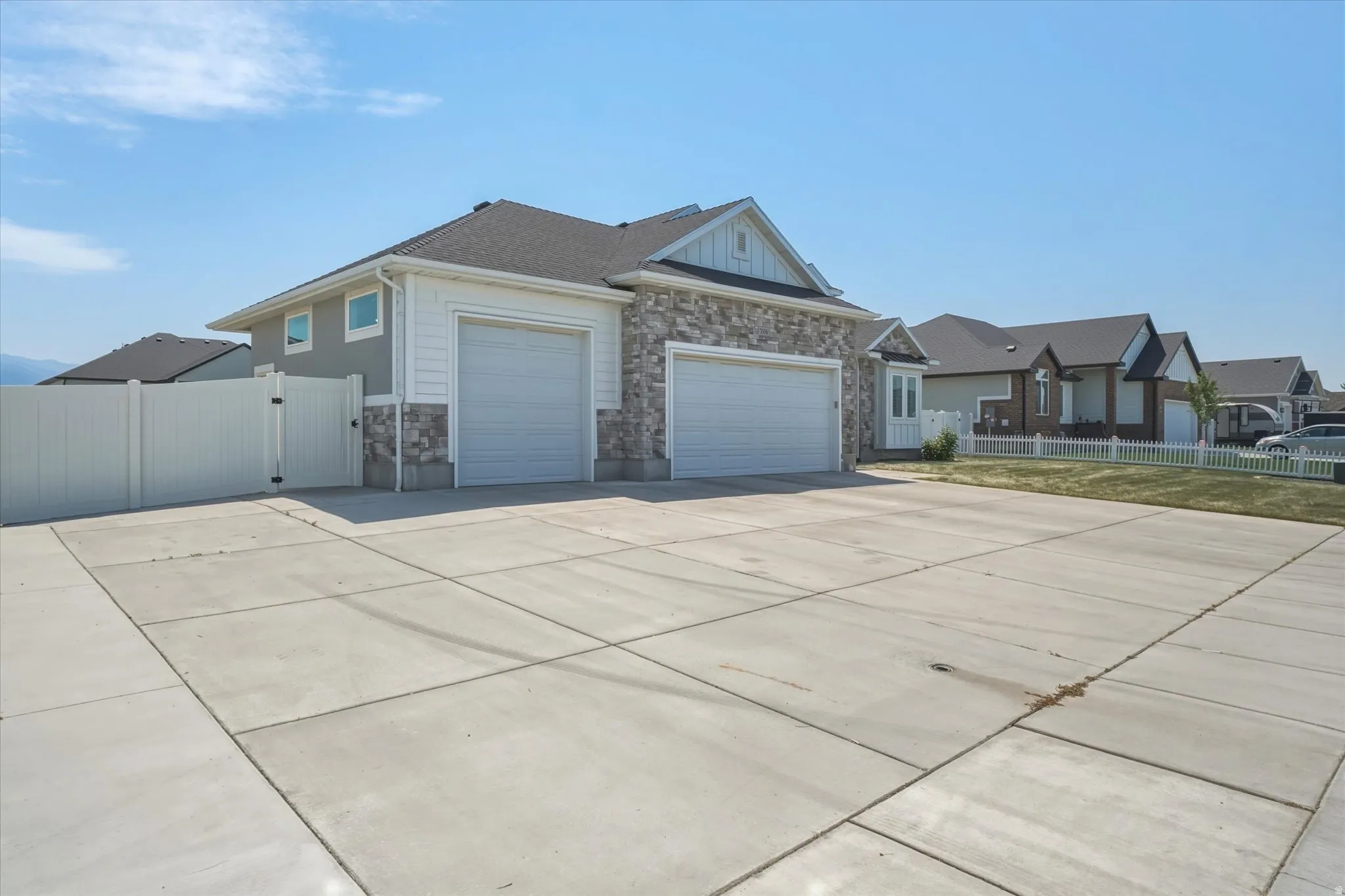 Exterior featuring a stone and siding facade, two garage doors, a concrete driveway, and a white privacy fence