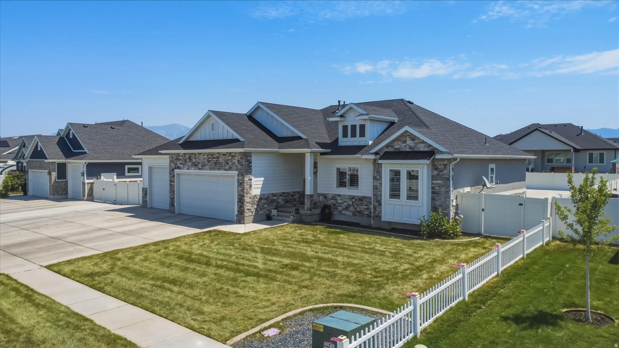 Contemporary residence featuring stone and siding exterior accents, a dark shingle roof, and multiple garage doors