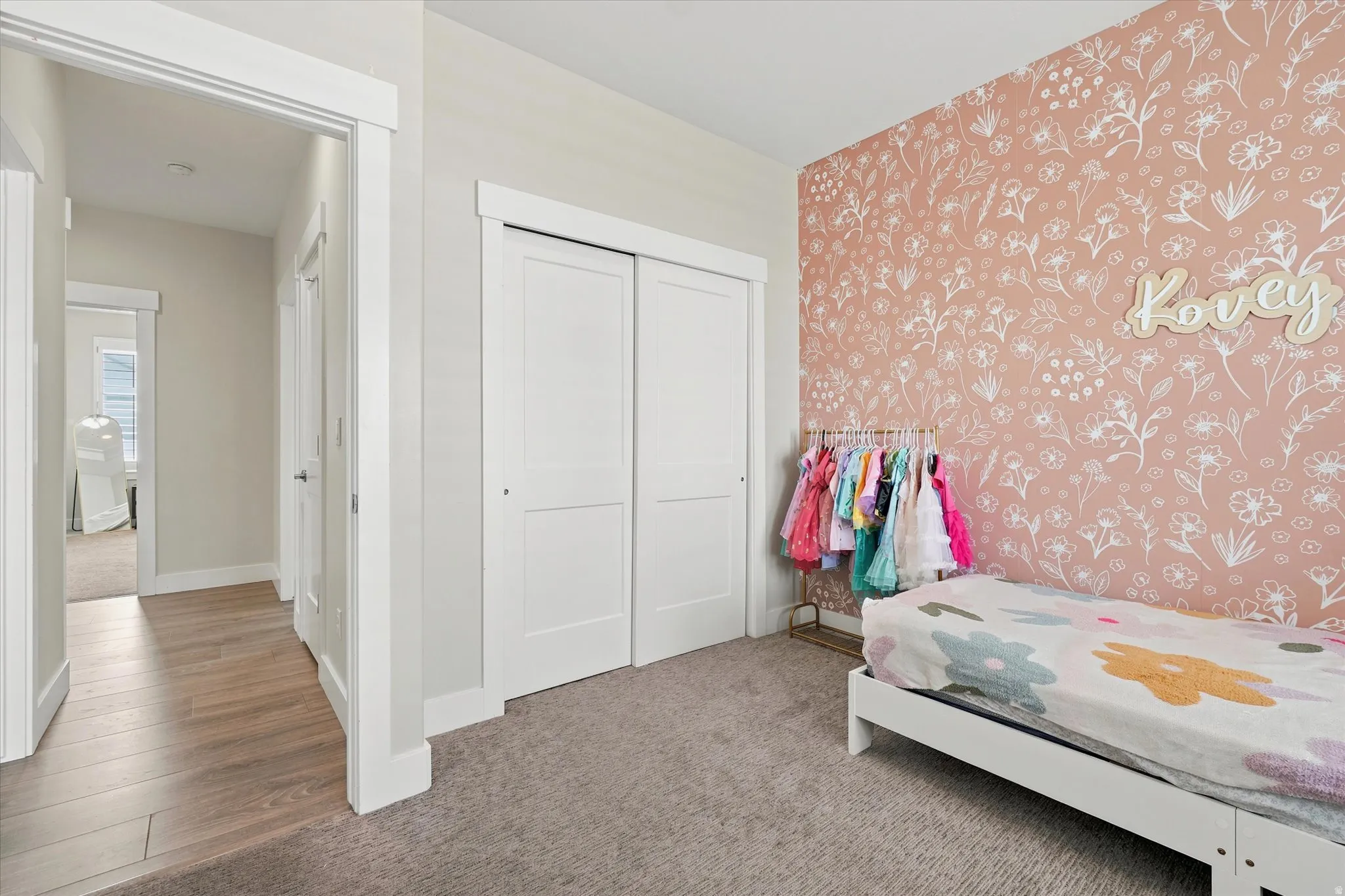 Bedroom featuring a floral accent wall, plush carpeting, and white sliding closet doors